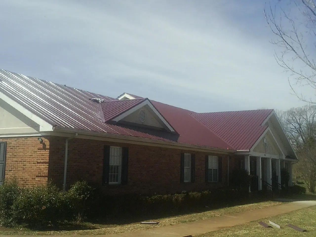 Red metal roof with gabled entries on a long brick building, from a Hail Damage Roof Repair job in Catawissa