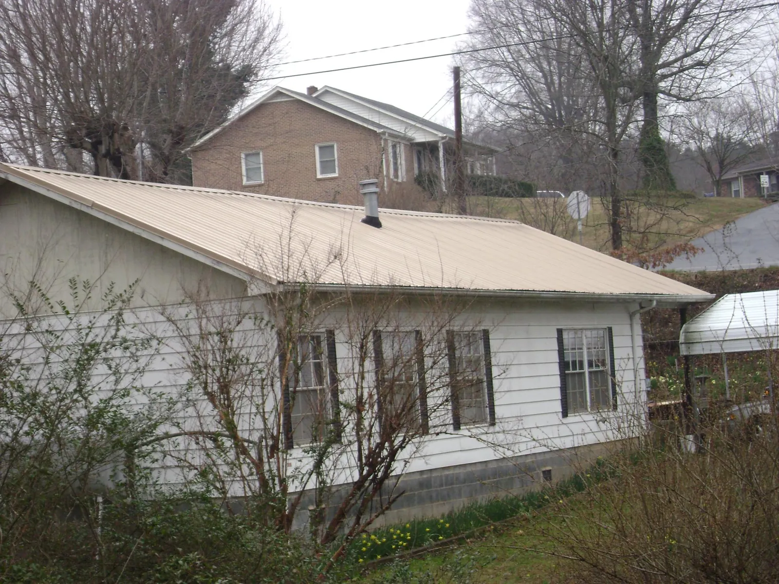 Tan metal roof on a white sided house set into a hillside — Commercial Roofing by Roofing Brothers in Catawissa
